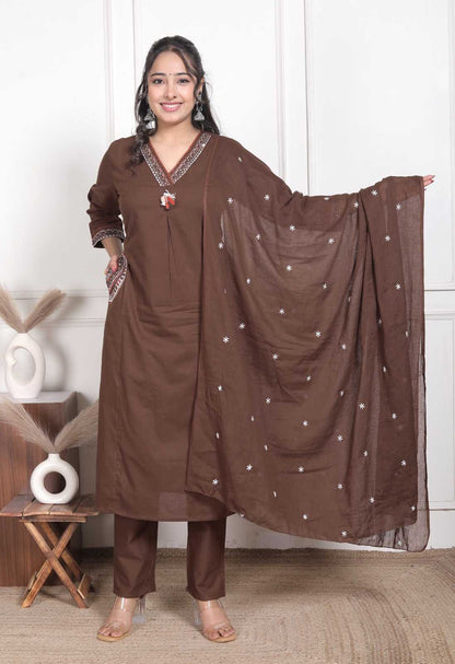 Woman wearing a brown traditional outfit with a scarf, standing indoors.