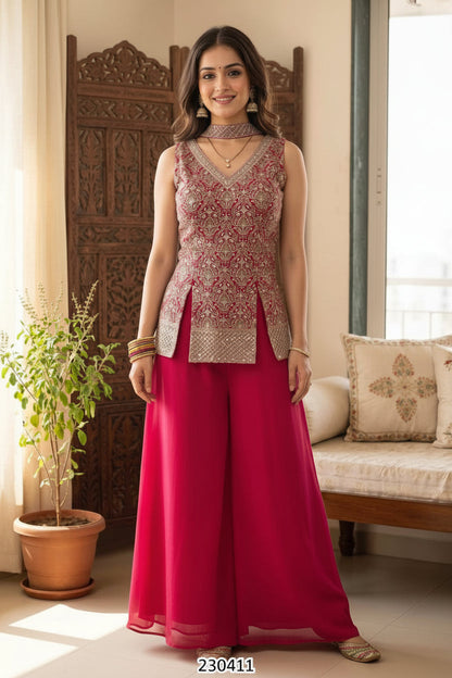 A woman modeling a traditional Indian outfit consisting of a sleeveless embellished top in beige and pink with bright pink wide-leg pants, standing in a decorated room with a carved wooden screen and a potted plant.