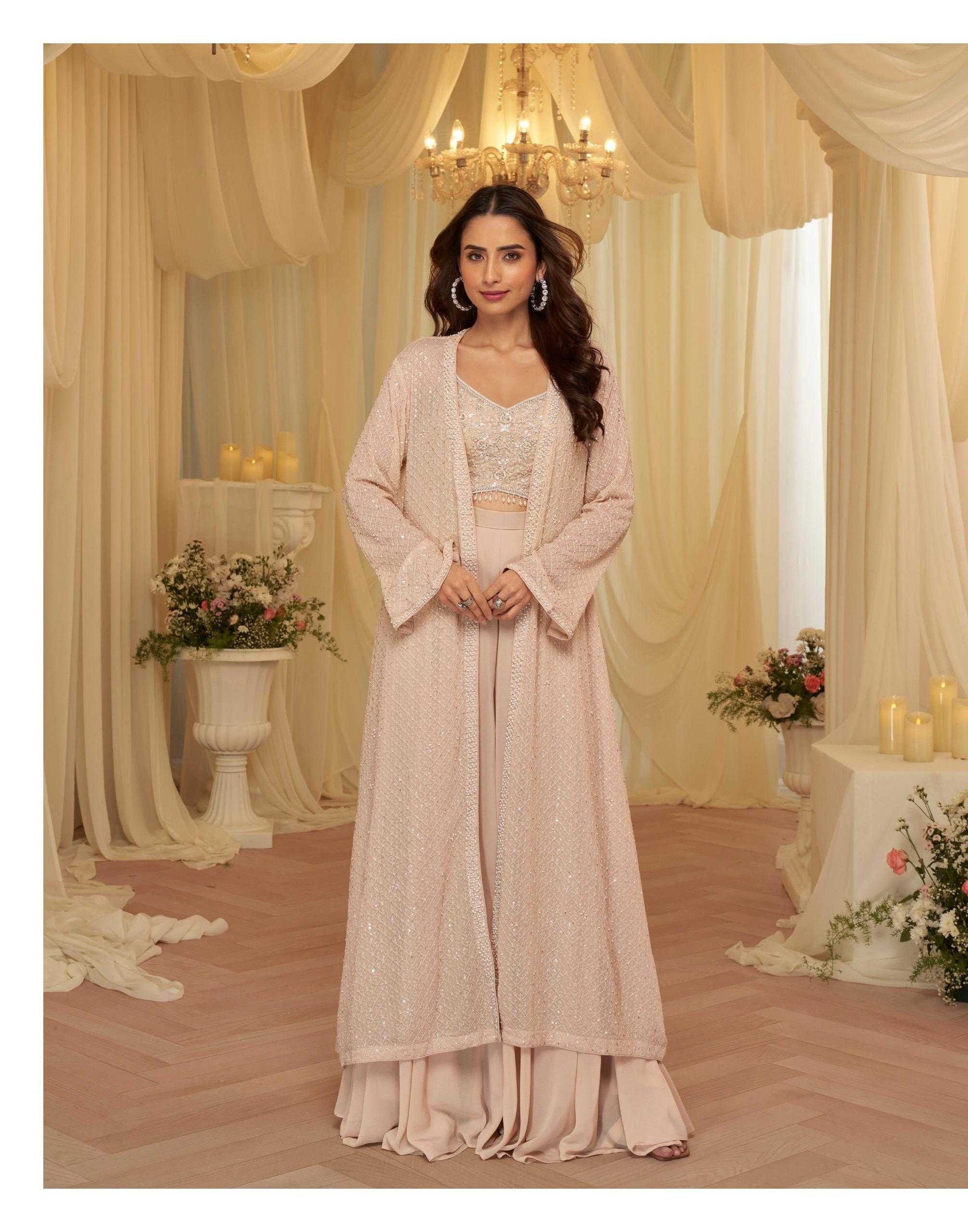 Woman in a beige traditional outfit standing in a decorated room with floral arrangements and candles.