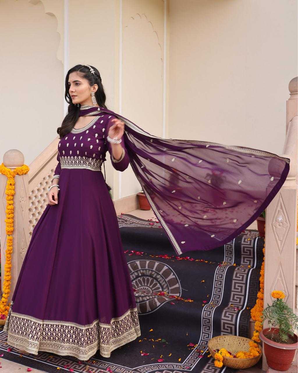 Woman in a purple traditional outfit with a flowing scarf in an indoor setting.