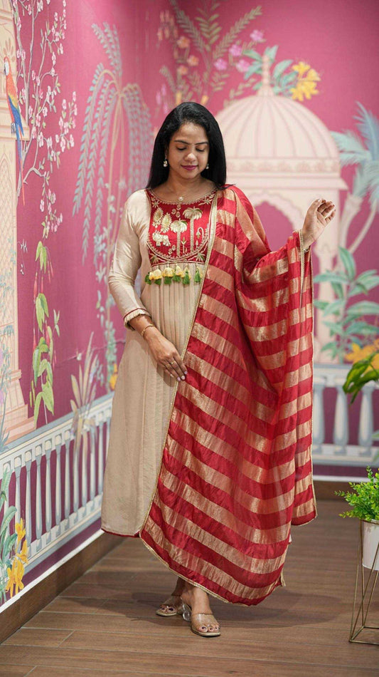 Woman in traditional outfit with red and gold dupatta against a colorful wall.