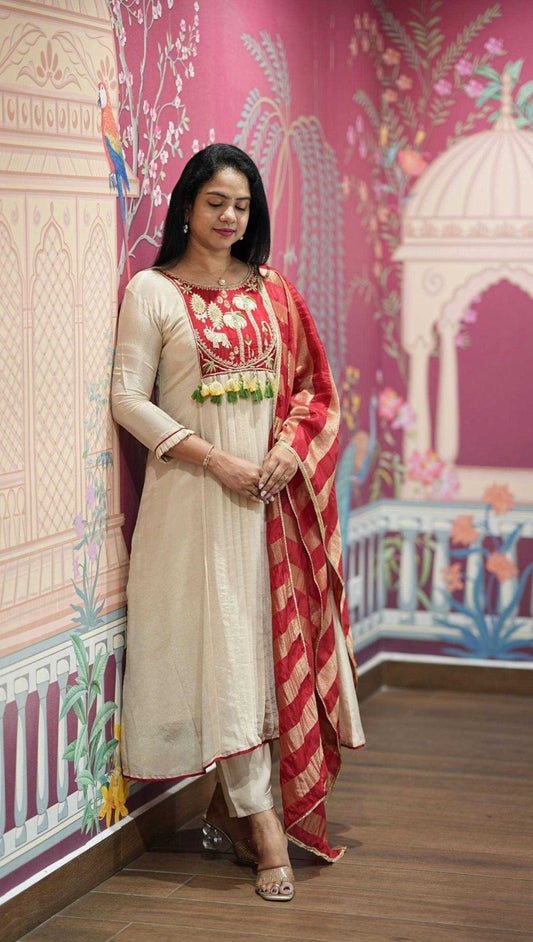 Woman in a traditional outfit standing against a decorated wall with colorful patterns.