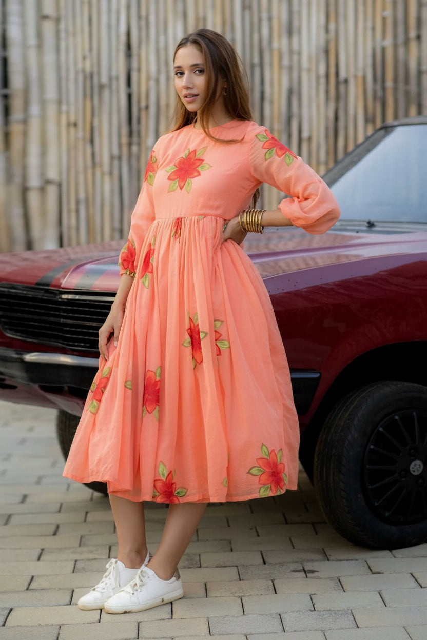 Woman wearing a peach dress with floral patterns standing next to a red car.
