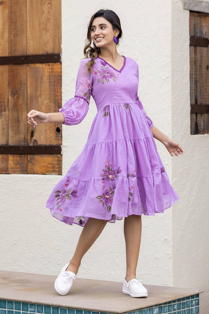 Woman wearing a purple embroidered dress standing against a wooden door and white wall.