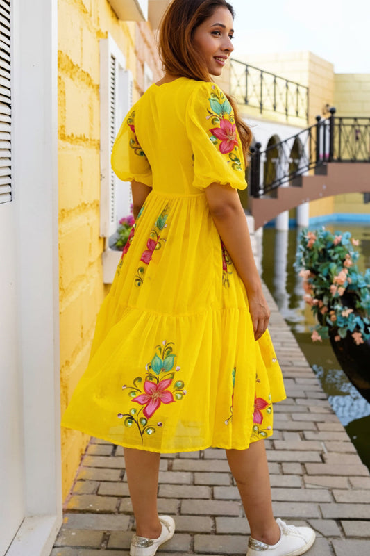 Woman wearing a yellow dress with floral embroidery in an outdoor setting.