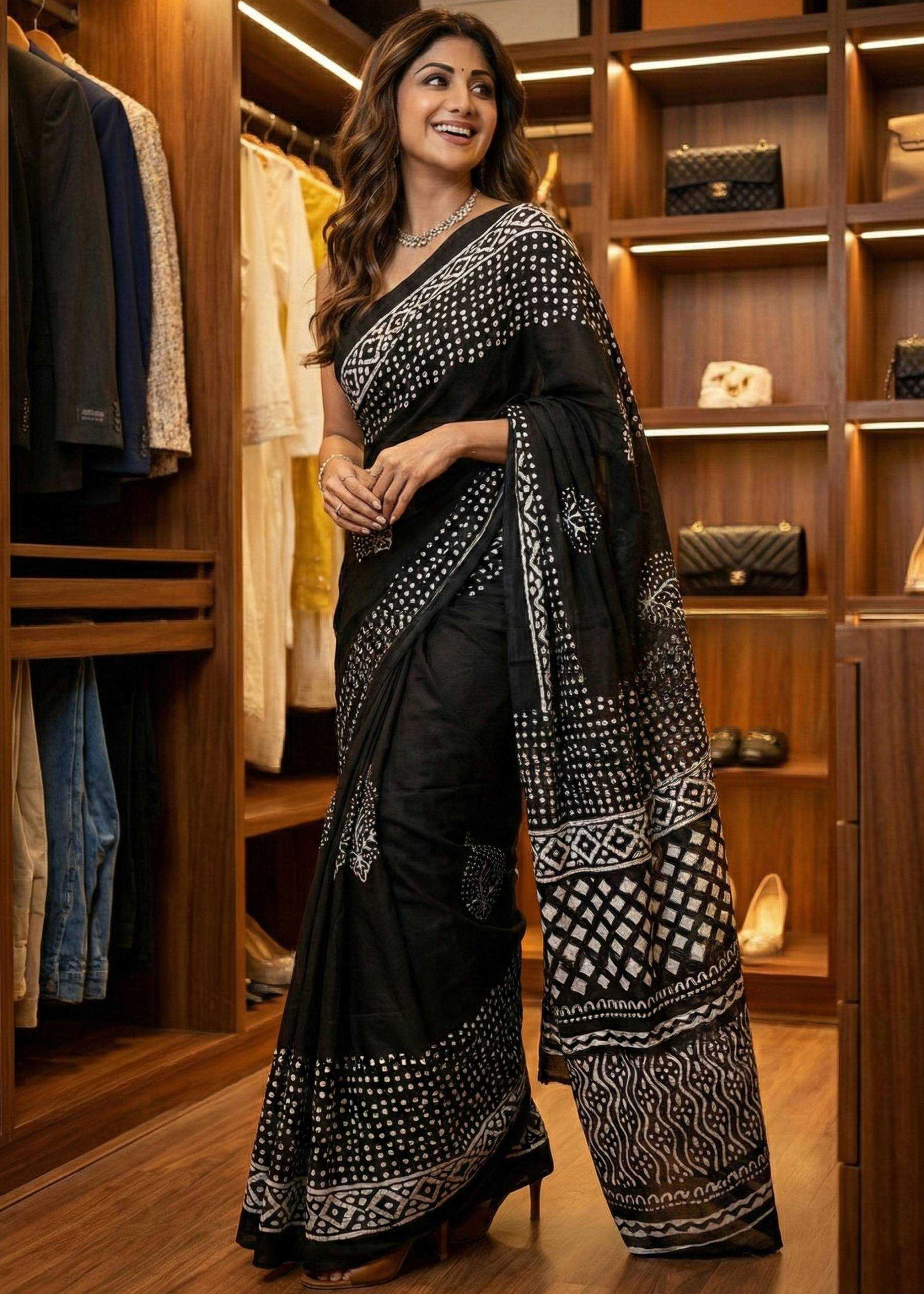 Woman in a black and white saree standing in a wardrobe with clothes and bags.