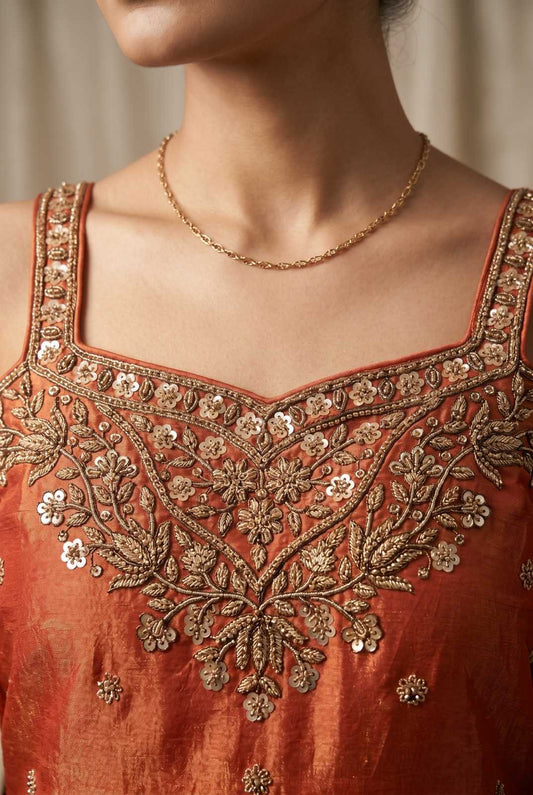 Close-up of a person wearing an orange embroidered top with gold detailing.