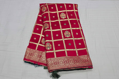 A folded red silk saree with gold zari grid patterns, floral motifs, and a decorative border, displayed on a white fabric background. The brand name 'Rani' is printed in white text across the center.
