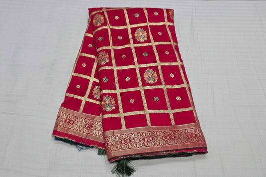 A folded red silk saree with gold zari grid patterns, floral motifs, and a decorative border, displayed on a white fabric background. The brand name 'Rani' is printed in white text across the center.
