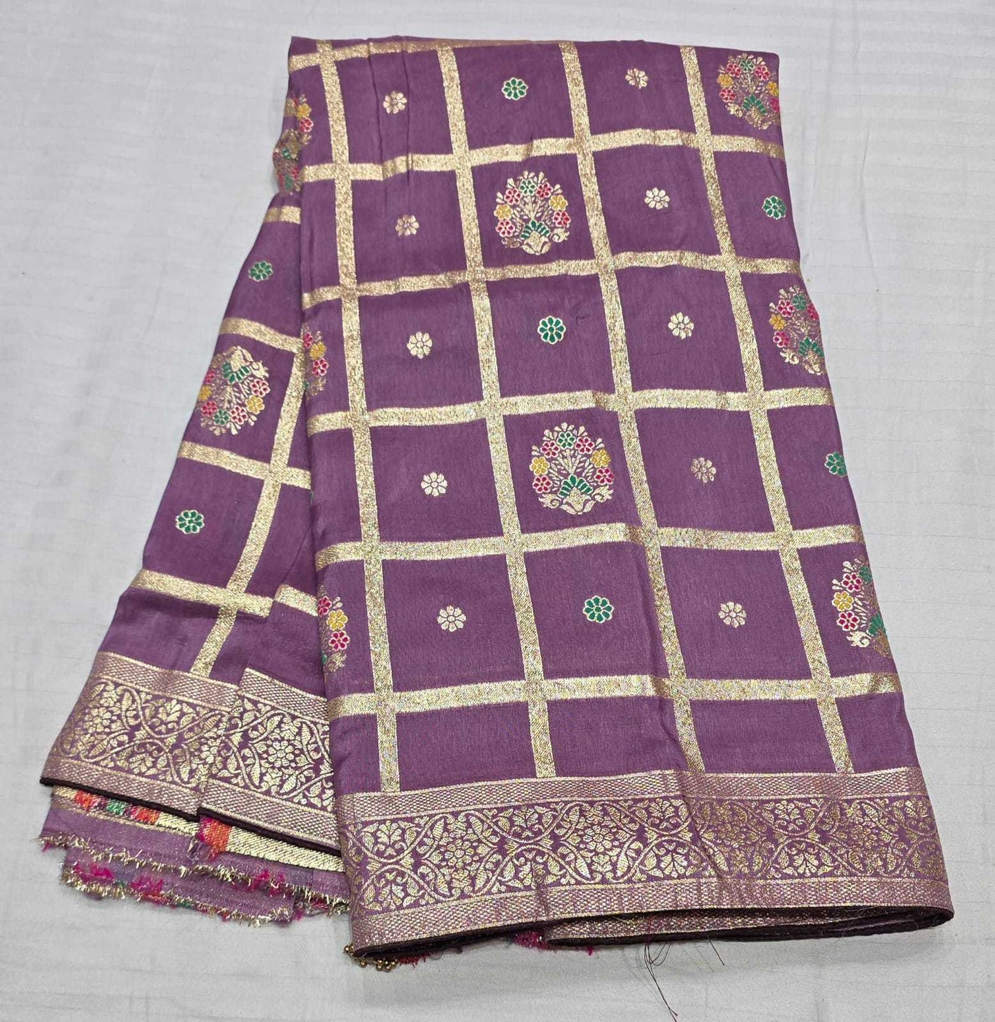 Purple silk saree with gold zari grid pattern, floral motifs, and a decorative gold border, folded on a white background.