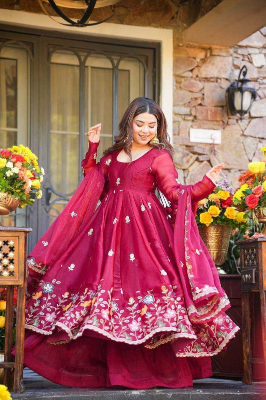 Woman in a red traditional outfit standing outdoors with floral decorations.